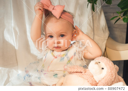 baby in beautiful dress takes off bow from her head baby in beautiful dress takes off bow from her head 88907472