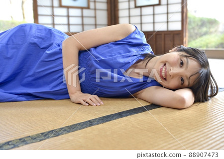 在日式房間的榻榻米墊上,一位身穿藍色連衣裙的微笑年輕女子 在日式房間的榻榻米墊上,一位身穿藍色連衣裙的微笑年輕女子 88907473