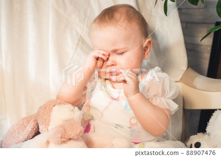 baby sits crying and rubbing her eyes with her hands baby sits crying and rubbing her eyes with her hands 88907476