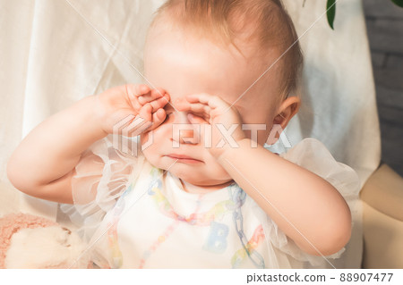 baby sits crying and rubbing her eyes with her hands 88907477
