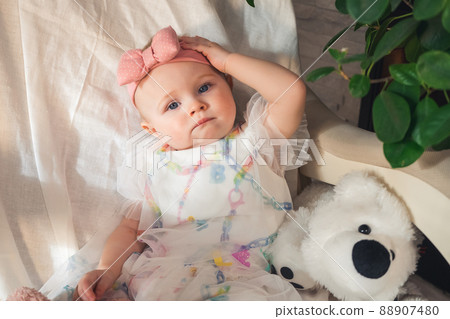 serious little girl in beautiful dress sits on an armchair and looks at camera serious little girl in beautiful dress sits on an armchair and looks at camera 88907480