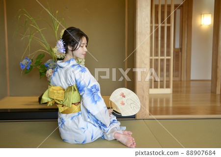 The back of a beautiful young woman in a yukata sitting on a tatami mat and relaxing with a fan in her hand The back of a beautiful young woman in a yukata sitting on a tatami mat and relaxing with a fan in her hand 88907684