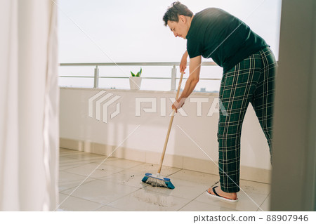 Man wiping floor with the mop. Janitor male washing the dirty floors. Guy mopping the balcony on a sunny day. Person doing home chores. Young fellow using cleaning equipment to dust the surface 88907946