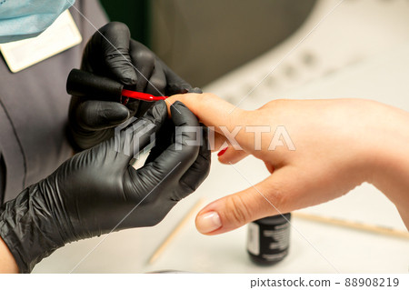 Manicure varnish painting. Close-up of a manicure master wearing rubber black gloves applying red varnish on a female fingernail in the beauty salon 88908219