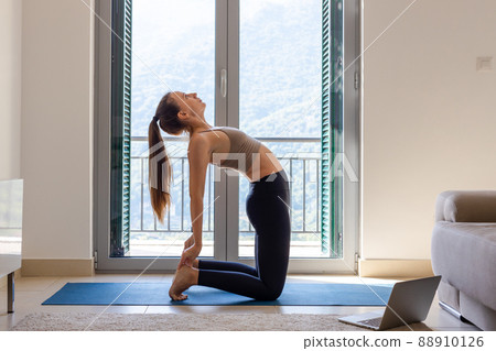 Young woman doing yoga practice on online class in the morning at home Young woman doing yoga practice on online class in the morning at home 88910126