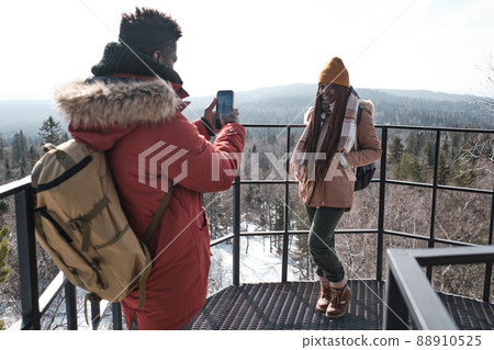 Young Black male tourist standing at observation deck on mountain top taking photos of his beautiful girlfriend 88910525