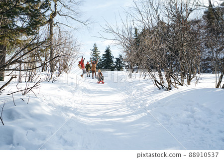 Extreme long shot of three young people having fun on winter day watching their friend sledding down Extreme long shot of three young people having fun on winter day watching their friend sledding down 88910537