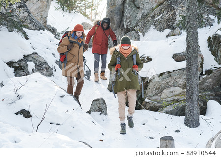 Group of three active young people wearing backpacks walking down the mountain on winter day Group of three active young people wearing backpacks walking down the mountain on winter day 88910544