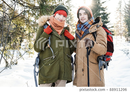 Horizontal medium portrait of active young Caucasian man and woman wearing backpacks posing on camera while hiking on winter day 88911206