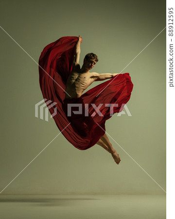 One young muscled man, flexible ballet dancer in action with red fabric, cloth isolated on olive color background. Theater, emotions, grace, art, beauty concept. One young muscled man, flexible ballet dancer in action with red fabric, cloth isolated on olive color background. Theater, emotions, grace, art, beauty concept. 88912595