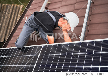 Man technician mounting photovoltaic solar moduls on roof of house. Electrician in helmet installing solar panel system outdoors. Concept of alternative and renewable energy. Man technician mounting photovoltaic solar moduls on roof of house. Electrician in helmet installing solar panel system outdoors. Concept of alternative and renewable energy. 88914890