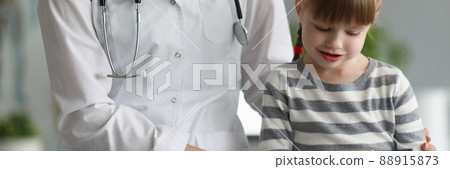 Doctor sits next to little girl holding clipboard 88915873