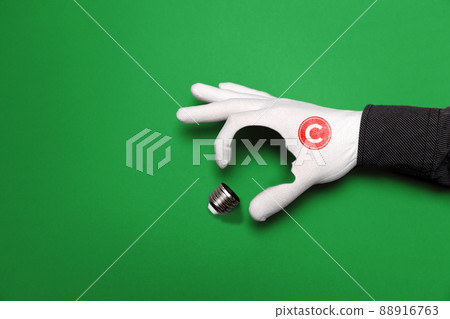 International Intellectual Property Day. A hand in a white glove with a copyright sign, depicts a light bulb, with the outline of a human face. Green background. The concept of copyright and ideas 88916763