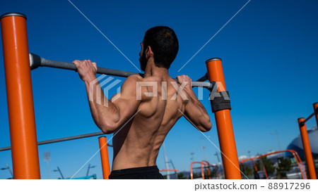 Shirtless man pulling up on horizontal bar outdoors. Shirtless man pulling up on horizontal bar outdoors. 88917296