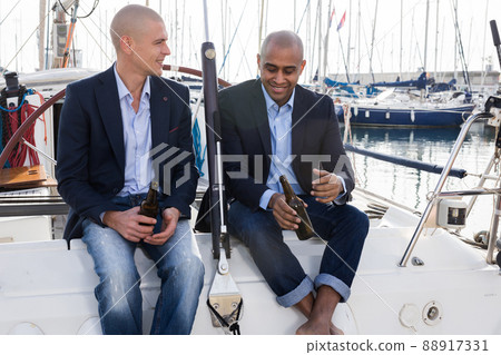 Latin American and European businessmen sit and drink beer on the yacht in seaport Latin American and European businessmen sit and drink beer on the yacht in seaport 88917331