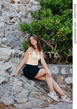 Beautiful girl sits on the stone wall of the old town of Budva . The girl sits on a stone parapet, Budva, Montenegro 88917492