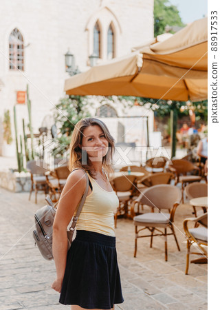 Girl Tourist Walking Through Ancient Narrow Street On A Beautiful Summer Day In MEDITERRANEAN MEDIEVAL CITY, OLD TOWN BUDVA, MONTENEGRO. Young Beautiful Cheerful Woman Walking On Old Street At 88917533