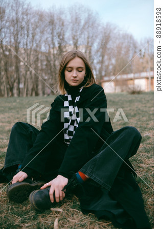woman in black coat sitting on the ground in the park woman in black coat sitting on the ground in the park 88918598