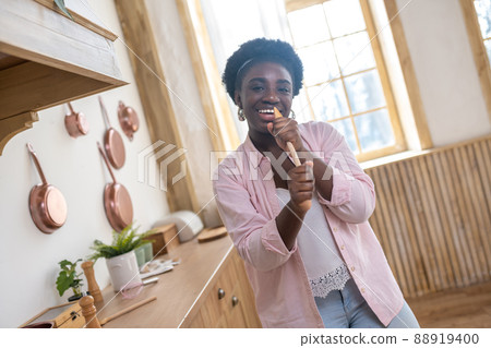 Contented african woman in pink clothes singing in the kitchen 88919400