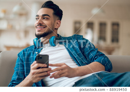 Young man in a blue tshirt with a phone in hands sitting on the sofa Young man in a blue tshirt with a phone in hands sitting on the sofa 88919450