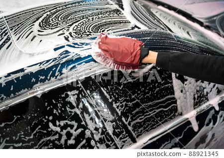 Professional car wash. Detailing worker washes the vehicle body with foam and rag Professional car wash. Detailing worker washes the vehicle body with foam and rag 88921345