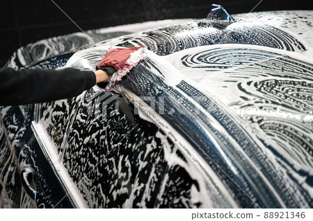 Professional car wash. Detailing worker washes the vehicle body with foam and rag 88921346