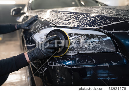 Man cleans car lamp with circle sponge. Preparing auto for polishing. .Detailed car wash 88921376
