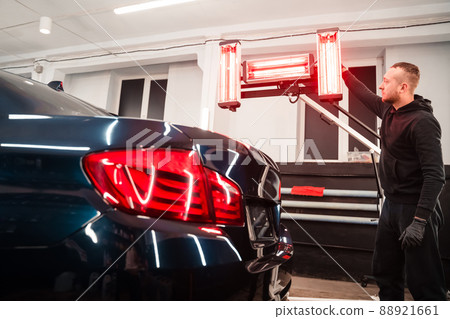 Detailing worker with infrared lamps near the car. Car detailing concept Detailing worker with infrared lamps near the car. Car detailing concept 88921661