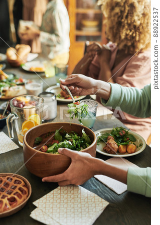 Close-up of boy putting fresh vegetable salad from bowl on his plate during dinner at table with his family Close-up of boy putting fresh vegetable salad from bowl on his plate during dinner at table with his family 88922537