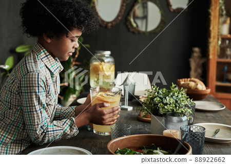 African little boy putting the jug with lemonade on table for holiday dinner in dining room 88922662