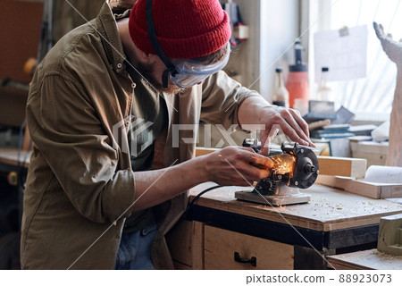 Professional young male carpenter wearing safety glasses working in joinery workshop sharpening knife using grinding jig Professional young male carpenter wearing safety glasses working in joinery workshop sharpening knife using grinding jig 88923073