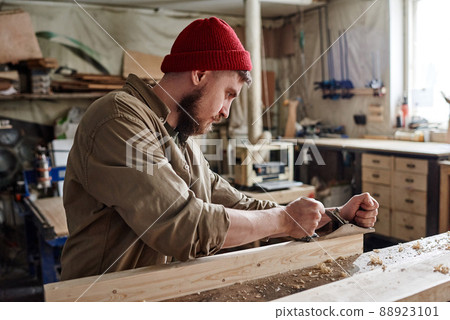 Modern young bearded Caucasian woodworker using hand plane to smooth and shape wooden plank Modern young bearded Caucasian woodworker using hand plane to smooth and shape wooden plank 88923101