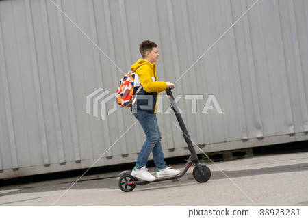 Modern teenager with backpack rides on electric scooter. Boy comes back from school 88923281