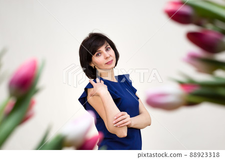 An adult brunette in a blue blouse on a white background with bright red juicy tulips An adult brunette in a blue blouse on a white background with bright red juicy tulips 88923318