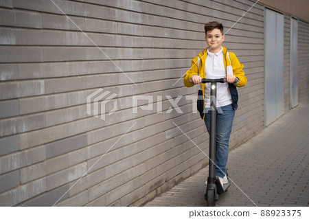 Handsome teenager rides on electric scooter down the city street Handsome teenager rides on electric scooter down the city street 88923375