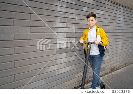 Handsome teenager rides on electric scooter down the city street Handsome teenager rides on electric scooter down the city street 88923376