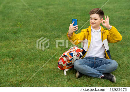 Teenager shows ok gesture while sitting on the lawn and talking on video call 88923673