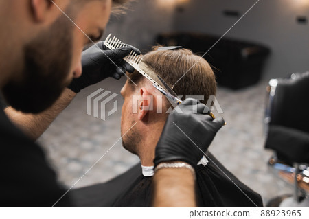 Hairdresser scissors hair on the head sides for a stylish black-haired man in the barbershop	 88923965