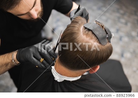 Hairdresser scissors hair on the head sides for a stylish black-haired man in the barbershop	 88923966