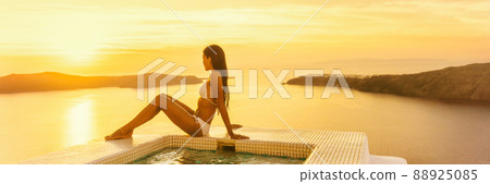 Luxury travel Santorini hotel woman by resort swimming pool at sunset - Bikini body model sunbathing banner panorama. 88925085