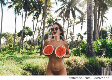 Cheerful woman with halved watermelon having fun in tropical garden 88925566