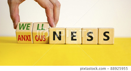 Wellness or anxiousness. Doctor turns cubes and changes the word 'anxiousness' to 'wellness'. Beautiful yellow table, white background. Psychological, wellness or anxiousness concept. Copy space. Wellness or anxiousness. Doctor turns cubes and changes the word 'anxiousness' to 'wellness'. Beautiful yellow table, white background. Psychological, wellness or anxiousness concept. Copy space. 88925955