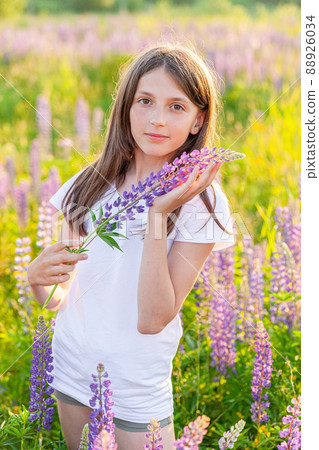 Happy teenage girl smiling outdoor. Beautiful young teen woman resting on summer field with blooming wild flowers green background. Free happy kid teenager girl, childhood concept 88926034