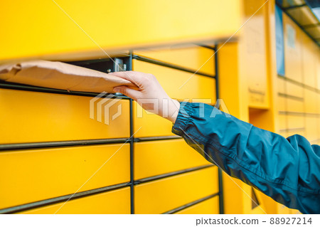 Hand with package. Send or receive parcel with yellow self service post terminal machine.  88927214