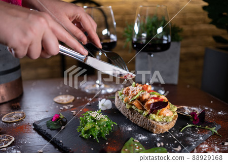 person eats fresh sandwich with avocado, red salmon fried fish, seaweed, wine 88929168
