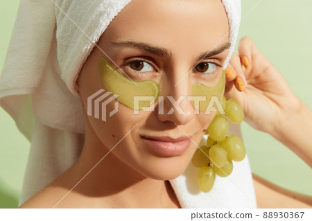 Woman using grapeseed-based eye patches on pastel green background. Natural sustainable skincare 88930367