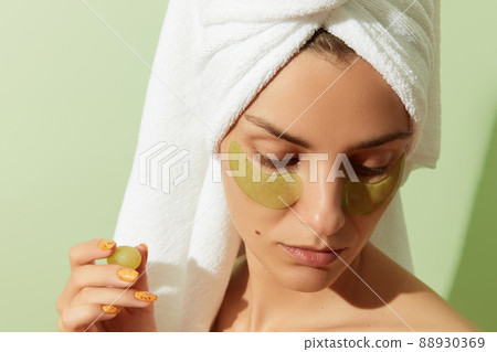 Woman using grapeseed-based eye patches on pastel green background. Natural sustainable skincare 88930369