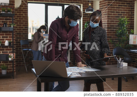 Multi ethnic diverse company business employees wearing masks against covid trying to solve financial issues. Expectant mother analyzing marketing strategy ideas while having clipboard in hand. Multi ethnic diverse company business employees wearing masks against covid trying to solve financial issues. Expectant mother analyzing marketing strategy ideas while having clipboard in hand. 88932035