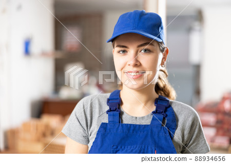 Smiling young female builder in blue uniform at construction site Smiling young female builder in blue uniform at construction site 88934656