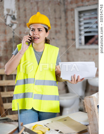 Young woman civil engineer with papers talking on phone at construction site Young woman civil engineer with papers talking on phone at construction site 88934748